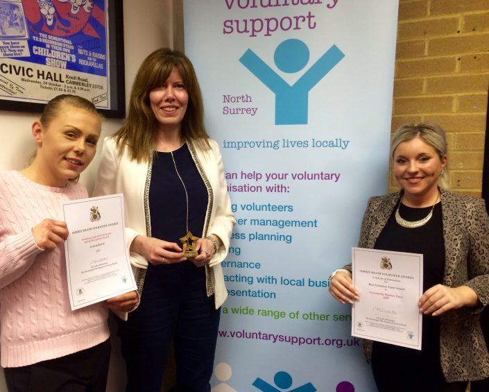 three women standing in front of a 'voluntary support' sign