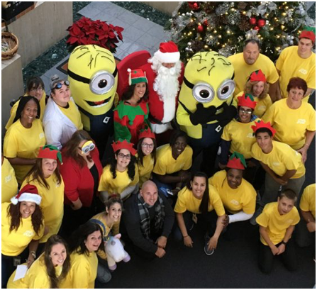 large group of ADP associates wearing yellow T-shirts surround Santa Claus, an elf, and two minion characters from the movie, Despicable Me.