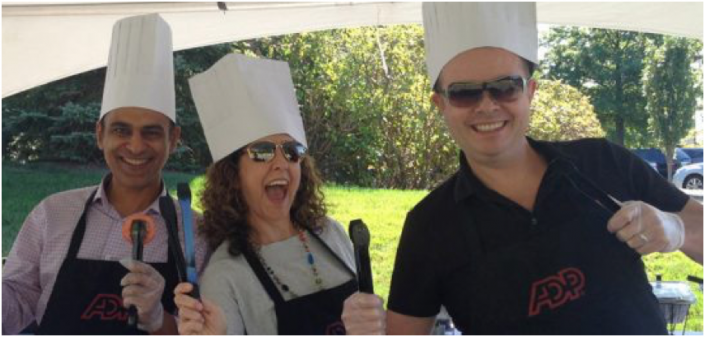 three ADP associates wearing chefs hats and holding BBQ utensils