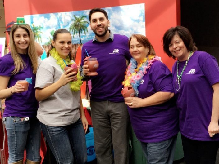 skupina zaměstnanců ADP ve fialových tričkách a s tropickými koktejly v rukou