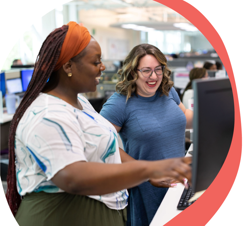 two women smiling at a workstation looking at a computer screen