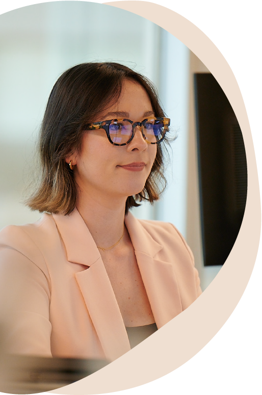 woman with short brown hair, glasses, and peach-color blazer looking at computer screen