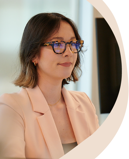 woman with short brown hair, glasses, and peach-color blazer looking at computer screen
